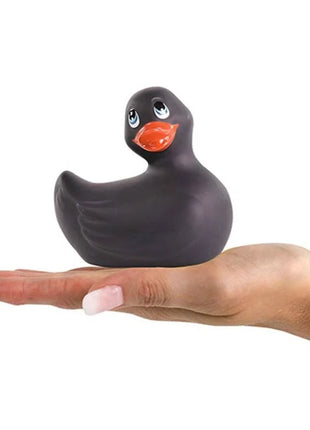 Ein glänzender schwarzer silikon-ente vibrator mit orangefarbenem schnabel und blauen augen von big tease toys in einer offenen hand