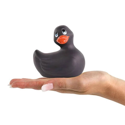 Ein glänzender schwarzer silikon-ente vibrator mit orangefarbenem schnabel und blauen augen von big tease toys in einer offenen hand