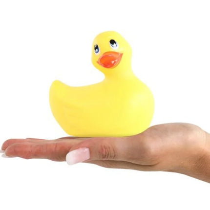 Ein klassische gelbe vibrierende Gummiente von Big Tease Toys mit schwarzen Augen und oranger Schnabel in einer Hand