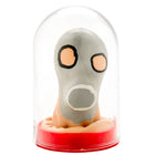 Graue cartoonartige gasmaske mit orangen augen und weißem mund, handbemalt, unter glaskuppel auf rotem sockel