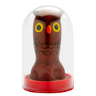 Eine braune schokoladeneulenfigur mit gelben augen und schwarzer gesichtszeichnung in einer klaren glaskuppel von condomerie