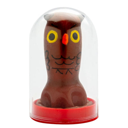 Eine braune schokoladeneulenfigur mit gelben augen und schwarzer gesichtszeichnung in einer klaren glaskuppel von condomerie