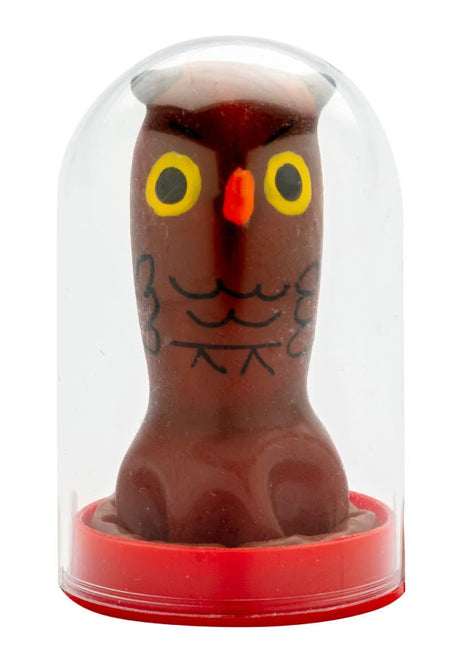 Eine braune schokoladeneulenfigur mit gelben augen und schwarzer gesichtszeichnung in einer klaren glaskuppel von condomerie