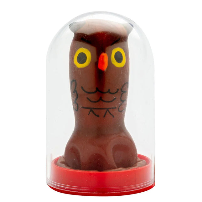 Eine braune schokoladeneulenfigur mit gelben augen und schwarzer gesichtszeichnung in einer klaren glaskuppel von condomerie