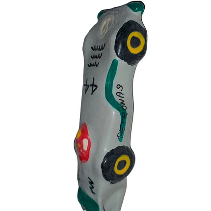 Graue keramik autofigur mit schwarzen und gelben rädern, grünen akzenten, rotem detail und petronas schriftzug, condomerie f1 mercedes xl