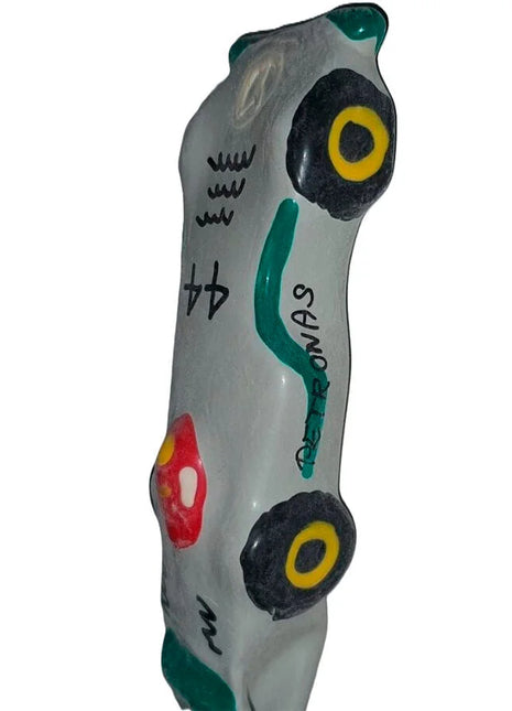 Graue keramik autofigur mit schwarzen und gelben rädern, grünen akzenten, rotem detail und petronas schriftzug, condomerie f1 mercedes xl