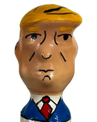 Ein glänzendes keramikfigürchen mit stylisiertem männlichen kopf, blonden haaren, blauem anzug und roter krawatte aus condomerie handbemalte neuheitskondome grumpy trump xl