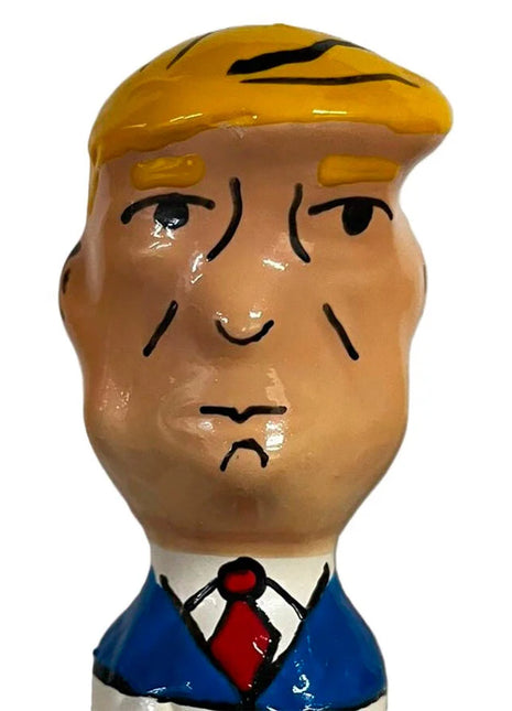 Ein glänzendes keramikfigürchen mit stylisiertem männlichen kopf, blonden haaren, blauem anzug und roter krawatte aus condomerie handbemalte neuheitskondome grumpy trump xl