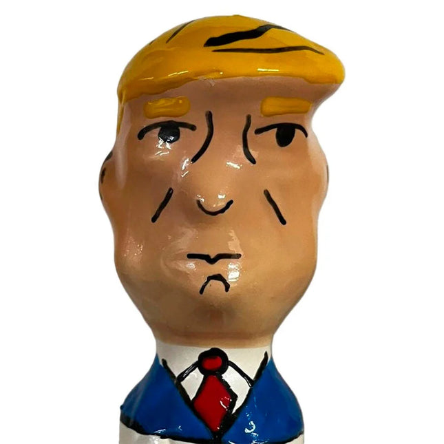 Ein glänzendes keramikfigürchen mit stylisiertem männlichen kopf, blonden haaren, blauem anzug und roter krawatte aus condomerie handbemalte neuheitskondome grumpy trump xl