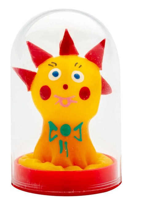 Eine gelbe plastikfigur mit roten spitzen und blauen augen in einer klaren glaskuppel auf rotem sockel von condomerie handbemalte neuheitskondome komet