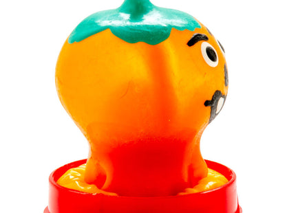Ein fröhliches orangenes und grünes plastikspielzeug pfeffer mit cartoon-gesicht auf rotem rundem sockel für condomerie handbemalte neuheitskondome kürbis