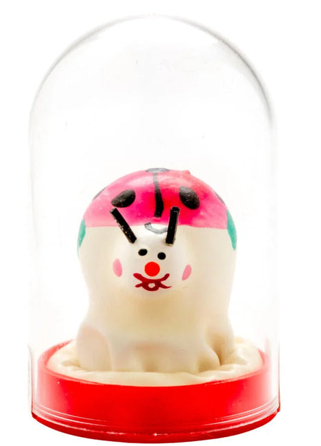 Eine handbemalte, cremefarbene marienkäfer-kondomfigur mit rosa-grünem kopfschmuck in einer glaskuppel von condomerie