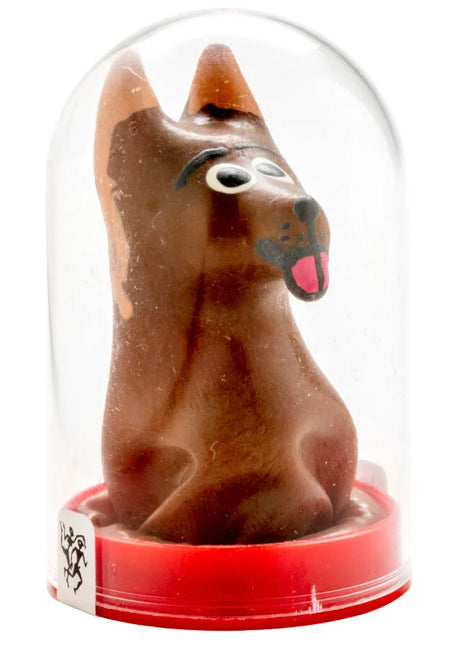 Eine braune schokoladenhundfigur mit schwarzen augen und rosa zunge unter einer klaren glaskuppel auf rotem ständer