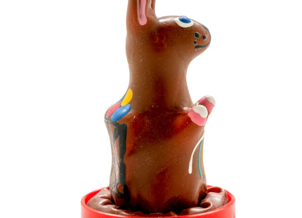 Eine handbemalte schokoladenosterhase mit rosa ohren, blauen augen und bunten bonbonverzierungen auf rotem plastiksockel