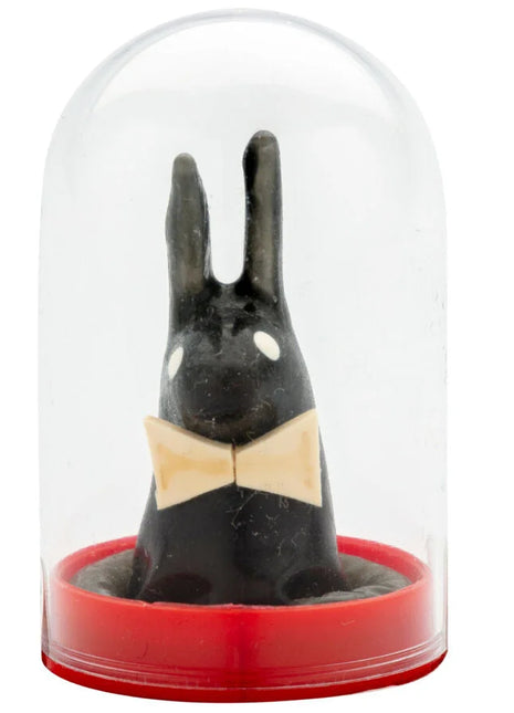 Schwarze hasenfigur mit weißen augen und beigem schleifenband unter glaskuppel auf rotem sockel von condomerie spielzeug kondome