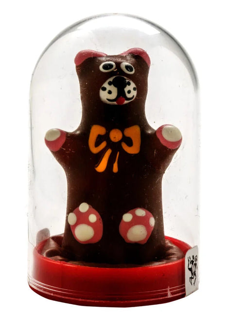 Handbemalte neuheitskondome teddybaer als schokoladenfigur mit rosa ohren, gepunkteten pfoten und gelber schleife unter glaskuppel auf rotem sockel