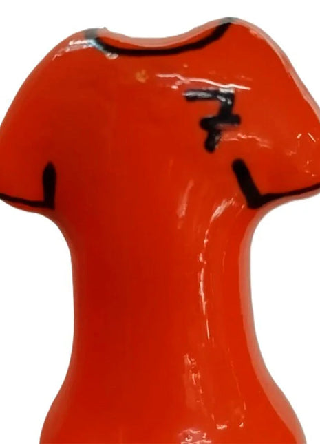Vibrante orange keramikfigur in t-shirt-form mit schwarzen details und stilisiertem logo auf der brust
