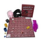 Rotes kama sutra spielbrett mit spanischem text und spielfeld umgeben von würfeln, bunten bechern, feder und schwarzem gürtel