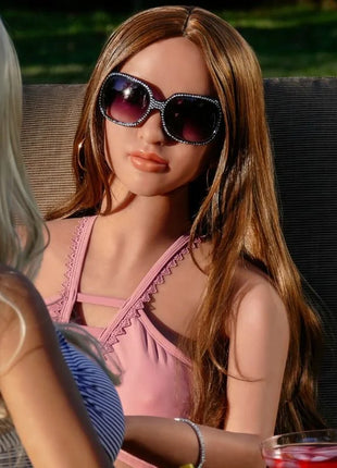 Eine frau mit langen braunen haaren trägt ein pinkes oberteil und große dunkle sonnengläser mit glitzersteinen bei pipedream extreme toys fantasy dolls carmen puppe 165 cm