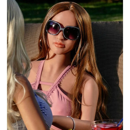 Eine frau mit langen braunen haaren trägt ein pinkes oberteil und große dunkle sonnengläser mit glitzersteinen bei pipedream extreme toys fantasy dolls carmen puppe 165 cm