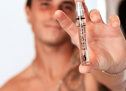 Eine klare glas-sprühflasche mit silberner kappe und schwarzem text eye of love pheromon parfum wird in der hand gehalten