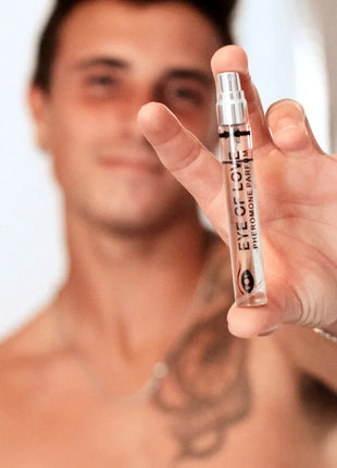 Eine klare glas-sprühflasche mit silberner kappe und schwarzem text eye of love pheromon parfum wird in der hand gehalten