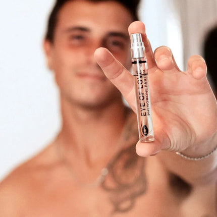 Eine klare glas-sprühflasche mit silberner kappe und schwarzem text eye of love pheromon parfum wird in der hand gehalten