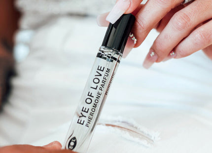 Ein klarer glas-roll-on-flakon mit schwarzem deckel labeled eye of love pheromon parfum wird zwischen zwei händen gehalten