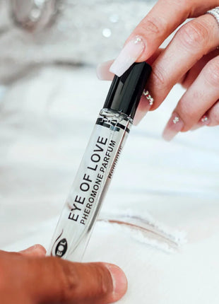 Ein klarer glas-roll-on-flakon mit schwarzem deckel labeled eye of love pheromon parfum wird zwischen zwei händen gehalten