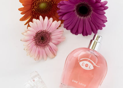 Ein pinkes glasparfum mit silberner sprühdüse und eol one love logo umgeben von bunten gerbera blumen