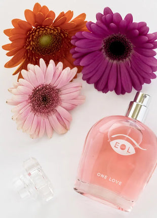Ein pinkes glasparfum mit silberner sprühdüse und eol one love logo umgeben von bunten gerbera blumen