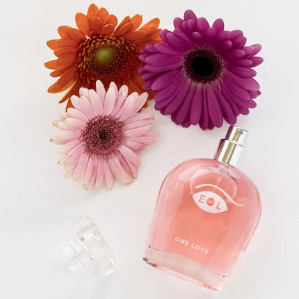 Ein pinkes glasparfum mit silberner sprühdüse und eol one love logo umgeben von bunten gerbera blumen