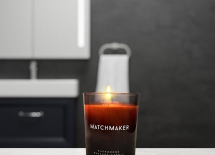 Ein brennendes bernsteinfarbenes pheromon-massagekerze in einem dunklen glas mit dem label matchmaker, 150 ml