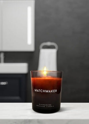 Ein brennendes bernsteinfarbenes pheromon-massagekerze in einem dunklen glas mit dem label matchmaker, 150 ml