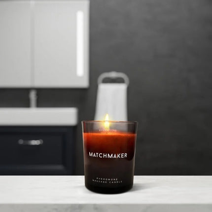 Ein brennendes bernsteinfarbenes pheromon-massagekerze in einem dunklen glas mit dem label matchmaker, 150 ml