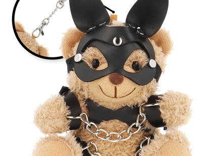 Ein tanfarbener plüsch-teddybär fetisch submissive mit schwarzer ledermaske, nieten, ohrstücken, schwarzem harness und silberner kette
