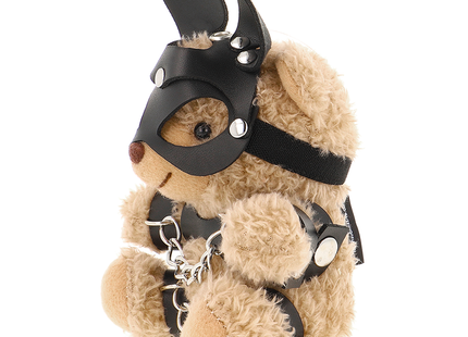 Ein plüschiger tanfarbener teddy bär im fetisch submissive stil mit schwarzer ledermaske, silbernen nieten und kettenharness