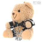 Ein plüschiger tanfarbener yohgi teddybär mit schwarzem ledergeschirr und silbernen kettensperren im bdsm stil