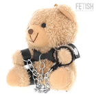 Ein plüschiger tanfarbener yohgi teddybär mit schwarzem ledergeschirr und silbernen kettensperren im bdsm stil