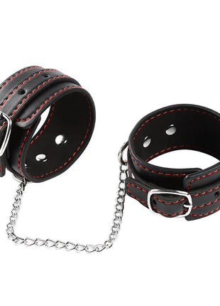 Schwarze leder handgelenkfesseln mit roter naht und silbernen metallschnallen verbunden durch eine kettensohle