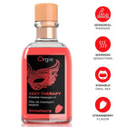 Eine klare glasflasche mit pfirsichfarbenem verschluss enthält pinkes erdbeer-aromatisiertes therapy kussmassageöl orgie