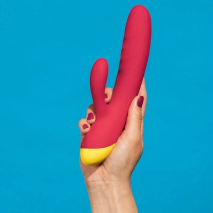 Ein vibrant roter und gelber silikon romp jazz rabbit-vibrator mit gebogenem schaft wird in der hand gehalten