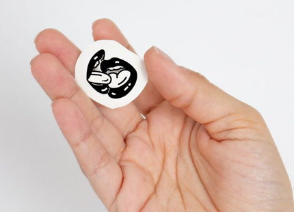 Weißer kreisförmiger aufkleber mit schwarzer illustration von zwei ineinandergreifenden stilisierten fröschen aus der spicy collection temporary tattoos