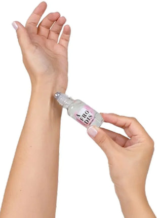 Ein klarer glas-rollerflakon mit rosa-weißem label aero dis wird auf das innere handgelenk gerollt secretplay afrodis parfümöl mit pheromonen für frauen 20 ml