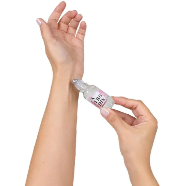 Ein klarer glas-rollerflakon mit rosa-weißem label aero dis wird auf das innere handgelenk gerollt secretplay afrodis parfümöl mit pheromonen für frauen 20 ml