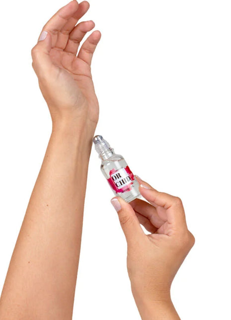 Eine klare glas-roll-on-flasche mit einem rosa-weißen etikett or chic wird von händen gehalten für secretplay orchideen-parfümöl mit natürlichen pheromonen 20 ml