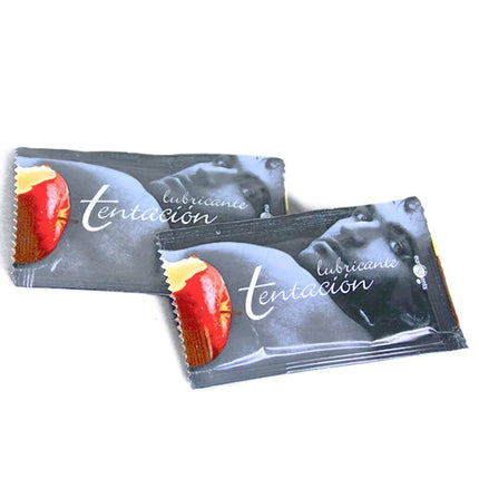 Zwei silberne einzeldosis-schmiermittel mit schokolade verpackungen von tentación mit rotem apfelmotiv und eleganter schrift